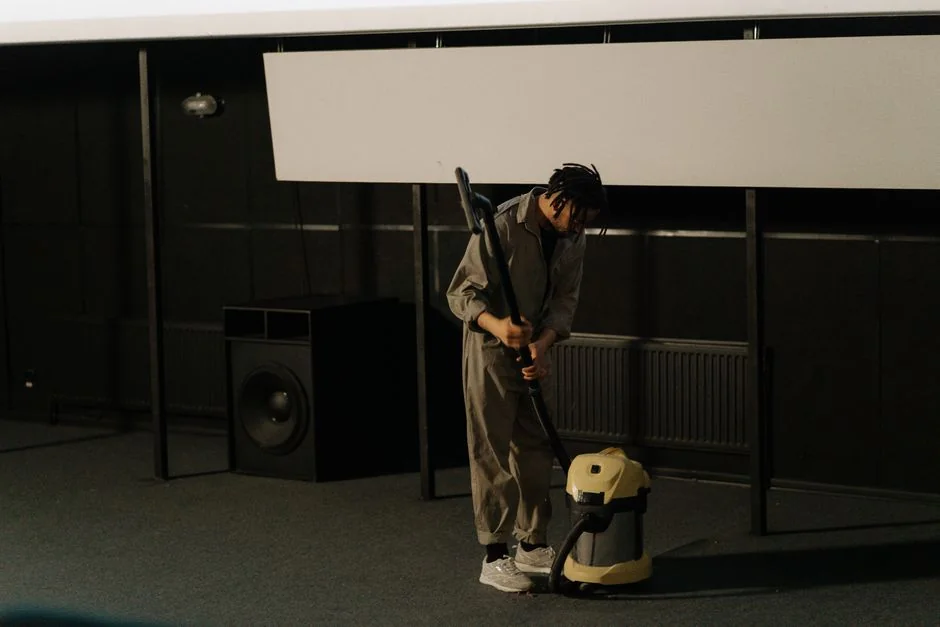 A professional cleaner in protective gear vacuuming the floor in a modern living room.